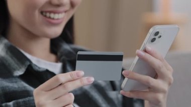 Yakın çekim kimliği belirsiz Asyalı kadın elinde banka kartı cep telefonu internet ödemeleri yapıyor e-ticaret alışveriş siparişleri alıyor web servisinde bağış yapıyor.