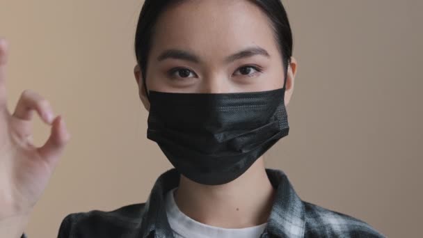 Ázsiai koreai japán kínai nő portré nő arc lány visel fekete arc orvosi védő maszk kovid pandémiás szabályok mutató ok gesztus finom jó szimbólum ajánlás jel nézi a kamera — Stock videók