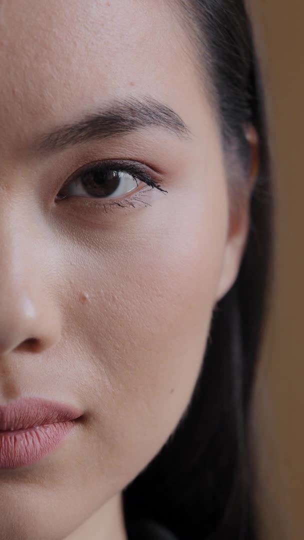 Vertikal vy asiatisk koreansk flicka ledsen kvinna hälften människa kvinnligt ansikte med mörka ögon naturlig makeup blinkande ser kamera feminism rasdiskriminering syn problem syn sjukvård kosmetologi — Stockvideo