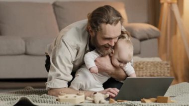 Bekar baba, sakallı baba, küçük kız çocuğu bebek bebek bebek evde oturup dizüstü bilgisayara bakıyor, internetten bilgisayar uygulaması kullanarak bebek ürünleri alıyor.