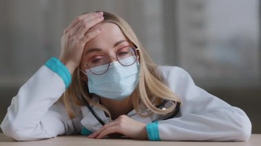 Ciddi üzgün, yorgun, beyaz kadın aşırı çalışan kadın doktor, doktor, hemşire, koruyucu maske üniforması giyen doktor, klinik hastanesinde üzgün bir şekilde oturuyor.