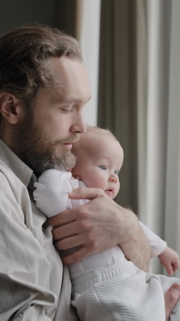 Dikey görüntü baba sakallı baba kucağında küçük kız çocuk bebek pencereden dışarı bak sabah adam ninni söylüyor çocuk bakımı aşk kavramı konuşuyor — Stok video