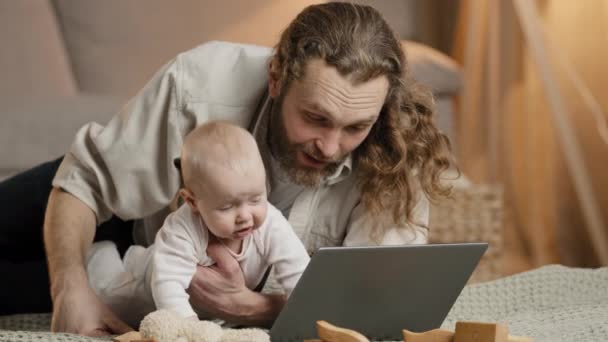 Caucásico padre barbudo con bebé recién nacido utiliza Internet portátil video llamada en línea conferencia chat en casa. Papá padre con hija pequeña hijo bebé mirada en la pantalla del ordenador niño jugar con juguete — Vídeo de stock