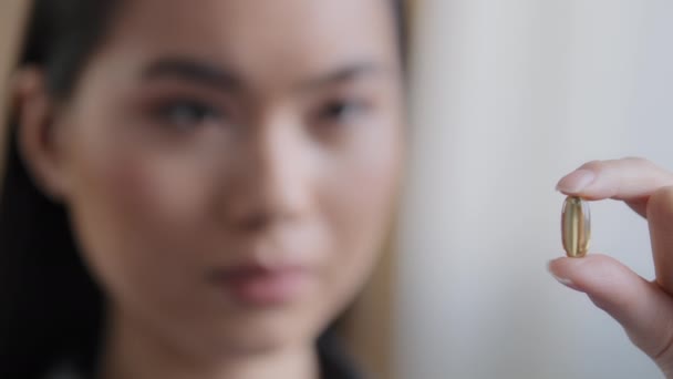 Extreme close-up weibliche verschwommenes weibliches Gesicht asiatisches Mädchen koreanische kranke Frau hält Vitaminpille hält Medikamentenkapsel gegen Mineralien Nahrungsergänzungsmittel. Gesundheitskonzept für gesunde Lebensqualität — Stockvideo