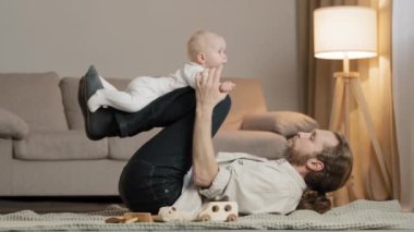 Mutlu erkek baba, beyaz baba, şirin küçük kızı kaldırıyor, oğlu uçuyor gibi yapıyor. Evde yerde yatıp eğleniyor gibi yapıyor. Sevimli küçük bebek bebekle babasıyla oynuyor.