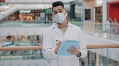 Genç Arap güvenlik müfettişi tıbbi maske ve bornoz denetleyicisi, araştırma yapan istatistiksel veri gözlemcisi yazısında doğruluk kontrolü yapar.