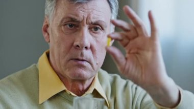 Elinde hap tutan yaşlı bir adamın portresi. Üzgün büyükbaba kapsüle bak. Ciddi, olgun, yaşlı bir emekli.