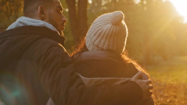Powrót widok zbliżenie młody para w miłość stojąc na zewnątrz w jesiennym parku patrząc na zachód słońca sunlight przytulanie korzystając romantyczny randka rozmowa spędzanie miło czas razem facet delikatnie przytula swoją dziewczynę — Wideo stockowe