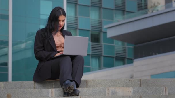 Młoda bizneswoman freelancer siedzi na zewnątrz pracując w Internecie wpisując na laptopie przy użyciu technologii komputerowej wykonując pracę online wysyłając klienta wiadomości tekstowych przez sieć przeglądania poczty e-mail wykorzystuje nową aplikację — Wideo stockowe