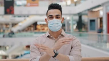Tıbbi maskeli genç İspanyol adam, Coronavirus salgını sırasında alışveriş merkezinin yasaklanması sırasında ciddi bir solunum cihazına sahip Arap 'ın davranışlarını yasaklıyor.