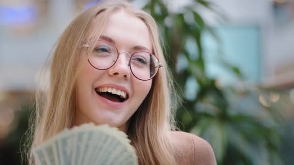 幸せな裕福な成功した女の子陽気な実業家カメラを見て女性豊かなライフスタイルドル紙幣の後ろに隠れてお金を費やしているお金を示しています。 — ストック動画