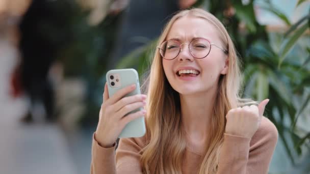 Happy euphoric young woman excited receive good news long awaited email message lady won lottery winner looking at phone cheerful girl celebrating victory dancing in mall successful female customer — Stock Video
