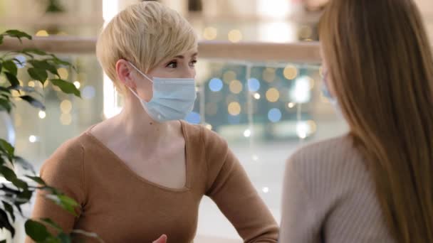 Dwie przyjaciółki matka z nastoletnią córką rozmawiającą w kawiarni noszą medyczne maski ochronne. Dorosła konsultantka po 40-tce doradza klientowi w pandemii. Kobieta w średnim wieku rozmawia z nierozpoznawalną dziewczyną — Wideo stockowe