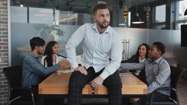 Kaukázusi gondolkodó fiatal férfi vezető ül az asztalon konferenciateremben magabiztos főnök mosolyog nézi kamera elégedett csapatmunka pozitív barátságos üzleti csapat megvitassák projekt csinál ötletbörze — Stock videók