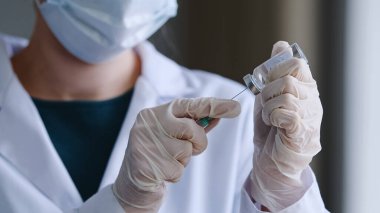 Koruyucu maskeli doktor kadının lateks eldivenli kadın elleri şırıngada sıvı ilaç antibiyotik aşısı koronavirüs ilacını arıyor aşı için hazırlayın.