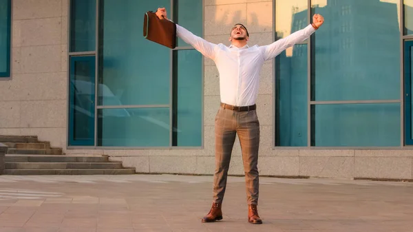 Успешный счастливый арабский бизнесмен бизнесмен босс предприниматель с портфелем поднять руки в воздухе стоя в городе рядом с современным зданием побеждает добиваться получает возможность новая работа делает победный жест — стоковое фото