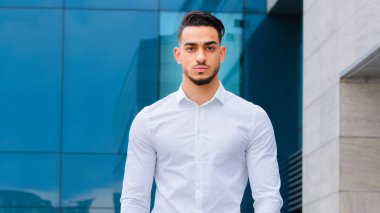 Ciddi Hispanik Arap Hintli işadamı modern binanın arka planında resmi giysiler içinde duruyor. Sokakta poz veren başarılı sakallı adam. Yakışıklı patron yönetici dışarıda.