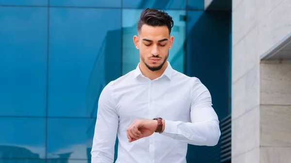 Serious upset angry hispanic indian man bearded guy disgruntled businessman boss wears formal stylish shirt stands outdoors looking at wrist watch worried about being late lateness time rush waiting — Stock Photo, Image
