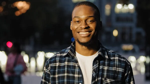 Portrait happy african american 20s millennial satisfied man guy stands in city in evening background looking at camera smiling toothy dental posing outdoors late time male face close up — Stock Photo, Image