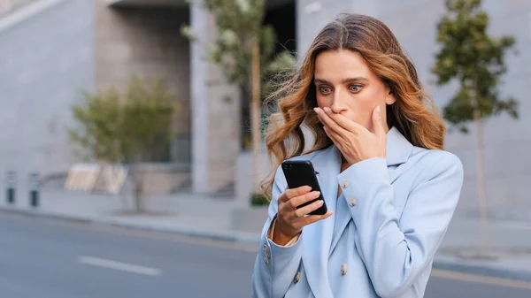 Femme d'affaires caucasienne à l'extérieur tenir téléphone mobile lire sms désagréables nouvelles terribles se sentent indignés couvre bouche visage choqué. Mauvais avis de compte bancaire bloqué cassé smartphone choc étonnement — Photo