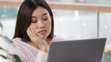 Üzgün üzgün bir kadın yüzü bıkkın bir Asyalı kadın yönetici kız öğrenci bilgisayarına bakıyor sabah ofiste çalışmaya çalışıyor sıkıcı çalışma tembelliği haberleri okuyor