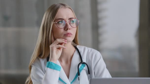 Enfocado caucásico mujer enfermera pensativa médico terapeuta en bata blanca sentado en la clínica del hospital pensando en la solución problema consejo médico profundo en pensamientos cuidado de la salud aplicación duda — Vídeo de stock