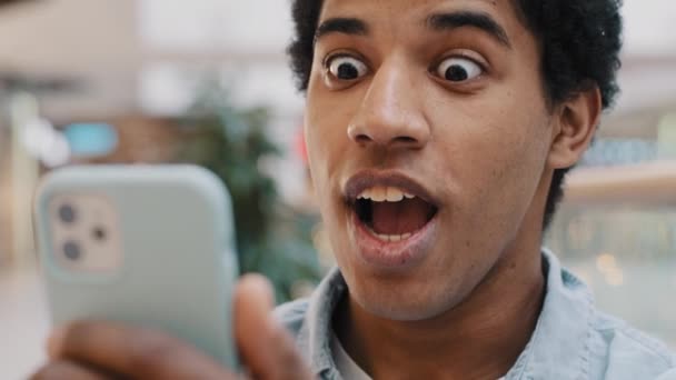 African happy excited guy surprised by message good news winning online bets looking at mobile phone has offer invite opens mouth in surprise delighted shock man feels amazing wonder with achievement — Stock Video