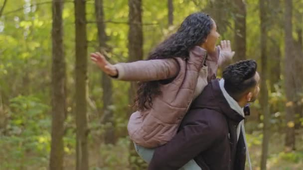 Ung fyr holder sin kæreste spinning glad pige sidder på kærester tilbage med arme ud til siden kramme smilende nyder tid tilbragt sammen romantisk date udendørs par forelsket gå i parken – Stock-video