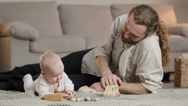 Счастливый взрослый отец помогает милой новорожденной дочке играть в игрушки вместе на полу заботливому отцу маленького мальчика девочки, весело играющего дома. Концепция развития ребенка — стоковое видео