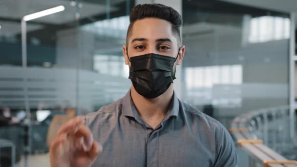 Close-up corporate business portrait arabian indian man wears black protective medical face mask observes precautionary measures looking at camera show ok sign hand gesture recommend pandemic rules — Stock Video