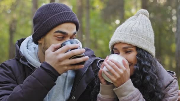 Close-up młoda para małżeńska turyści relaksujący się w przyrodzie w jesiennym lesie ocieplenie gorącym napojem pijąc ciepłą herbatę patrząc na siebie z uśmiechem miłości uczucie szczęśliwego przytulania ciesząc się wędrówką — Wideo stockowe
