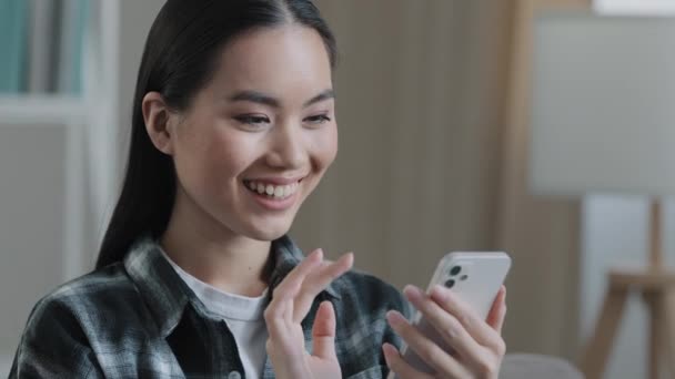 Главная портрет азиатки девушка блоггер глядя на экран мобильного телефона улыбаясь swipe проверки почты чата с бойфрендом выбирая продукт в Интернете в приложении для покупок счастливый клиент со смартфоном — стоковое видео