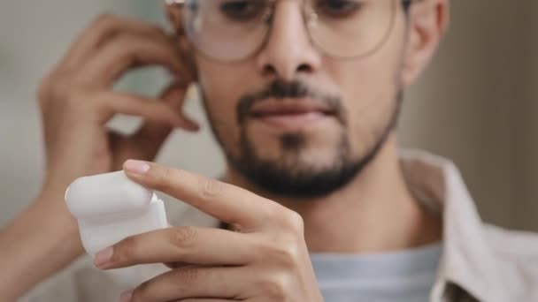 Gros plan mâle visage barbu arabe homme homme avec des lunettes ouvre la boîte avec écouteurs insère écouteurs sans fil dans les oreilles allume gadget écoute de la musique bénéficie audio strero son danse tête — Video