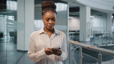 Afrika ciddi odaklı kadın ofis yöneticisi kadın patron modern akıllı telefonlu ofis şirketinin şirket uzay iş merkezinde kapalı mekanda daktilo yazan telefon. Telefon uygulaması olan iş kadını