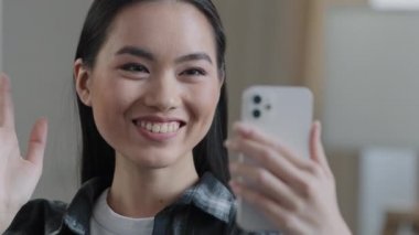 Mutlu Asyalı Çinli Çinli kız cep telefonuyla gülümseyen kadın yüzü kamerayla el sallıyor evde video görüşmesi yapıyor sanal video uygulaması ile sohbet ediyor.