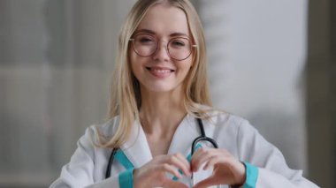Kafkas doktor uzman hemşire kadın pratisyen doktor masadaki klinik hastanesinde gözlük takıyor. Kalp şeklinde merhamet gösteriyor.