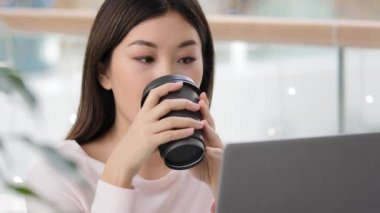 Portre sakin Asyalı kız kullanıcı blogger serbest yazar kadın dizüstü bilgisayarla internetten çay içerken kahve fincanından kapuçino içen kahve içen iş konuşmaları yapan iş konuşmaları yapan