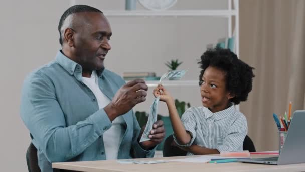 Famille afro-américaine assis au bureau adulte père professeur à domicile enseigne la littératie financière arithmétique petite fille apprend à compter avec de l'aide papier monnaie billets de dollar joyeux enfant joue avec papa — Video