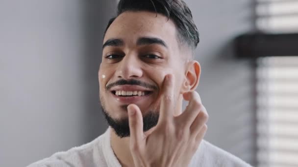Close-up männlich glücklich Gesicht mit perfekter Hautspiegel Ansicht hispanischen arabischen Mann bärtigen schönen gesunden Kerl lächelnd schmieren Wangen mit Feuchtigkeitscreme natürliche Anti-Falten-Gel nach der Rasur Schönheitsritual — Stockvideo