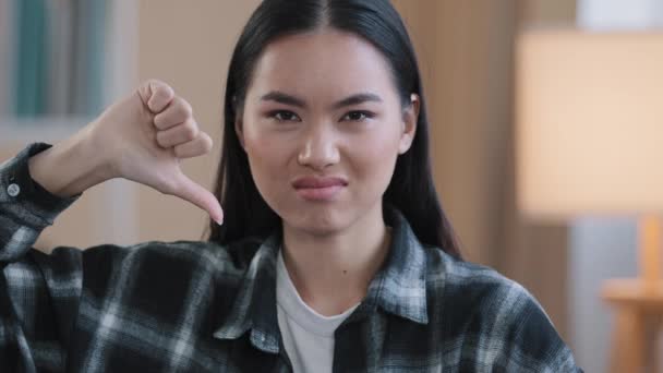 Close up asian millennial woman korean girl wear casual plaid shirt looking at camera showing dislike thumb down disagreement disgust rejection sign bad attitude gesture refusal failure symbol indoors — Stock Video