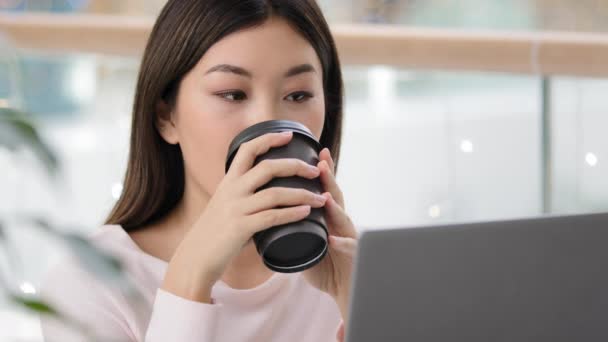 Porträtt lugn avslappnad asiatisk flicka användare bloggare frilansare student kvinna med bärbar dator titta på video på nätet dricka te kaffe cappuccino från papper kopp i café kontor företag chatta företag leende — Stockvideo