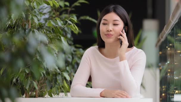 Asiatisk vänlig talande flicka sitter på café koreanska japanska kinesiska 20-talet kvinna fjärrpratar med pojkvän väntande datum svar samtal med mobiltelefon chatta med vän ler med gratis Wi-Fi — Stockvideo