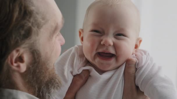 Mutlu beyaz kız bebek portresi yeni doğmuş kaygısız çocuk gülüşü aile zamanının keyfini çıkarır. Arkadan bakan sakallı baba kucağında küçük gülen bebek kahkahalarla gülen çocuk yüz ifadesi ebeveynlik. — Stok video
