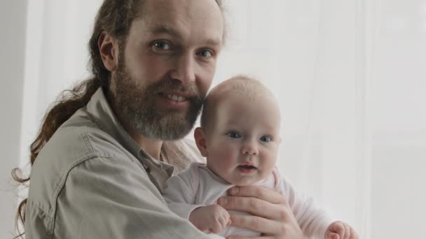 Ritratto di famiglia sorridente caucasico barbuto padre uomo abbracciando piccolo neonato ragazza ragazzo figlia figlio guardando la fotocamera sorridente posa a casa. Primo piano papà abbracciando bambino adottato — Video Stock