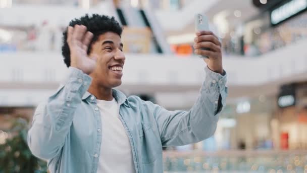 Retrato afro-americano cara estudante masculino dentro de casa usando celular aplicativo telefone acenando Olá falando vídeo chamada conferência bate-papo amigos conversa remota conversa distante comunicação com o smartphone — Vídeo de Stock