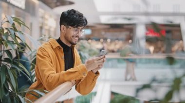 Mutlu gülümseyen genç Arap adam elinde telefonla flört sitesinde arkadaşlarıyla mesajlaşıyor akıllı telefondaki mobil uygulamayı kullanarak mesajlar yazıyor e-posta kontrolleri sosyal ağlar