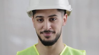 Ön cephedeki erkek müfettiş Arap adam tamirci mühendis işçi özel üniformalı, kasklı, gülümseyen, fotoğraf makinesi için poz veren İspanyol ustabaşı imalat çalışmalarından memnun.