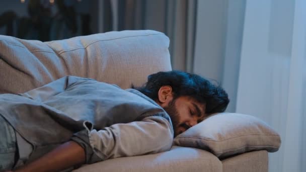 Vyčerpaný syndrom špatný pocit unavený arabský muž indický vousatý chlap pracovník muž doma padající tvář na gauči pohovka pozdě večer večer tmavý přepracovaný nemocný člověk nedostatek energie po party — Stock video