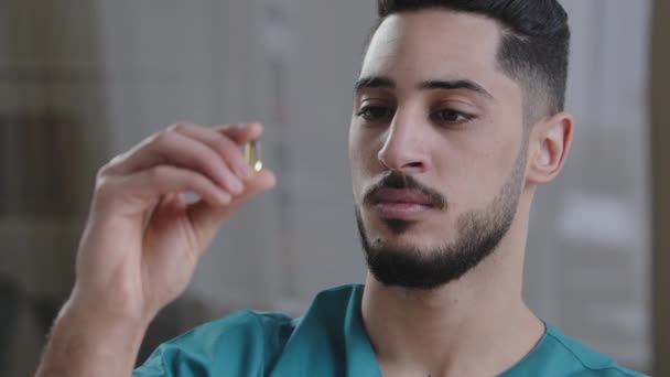 Joven científico hispano empleado médico hombre sosteniendo cápsula transparente clara tableta en mano análisis médico árabe estudiar las propiedades de la investigación clínica moderna droga en la industria farmacéutica — Vídeos de Stock