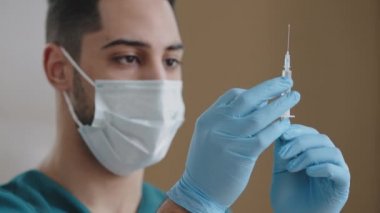 İspanyol doktor tıp cerrahı tıbbi maske takıyor. Eldivenleri doldurulmuş şırıngalara bastırıyor. İlaç köpükleri, sıvılar.